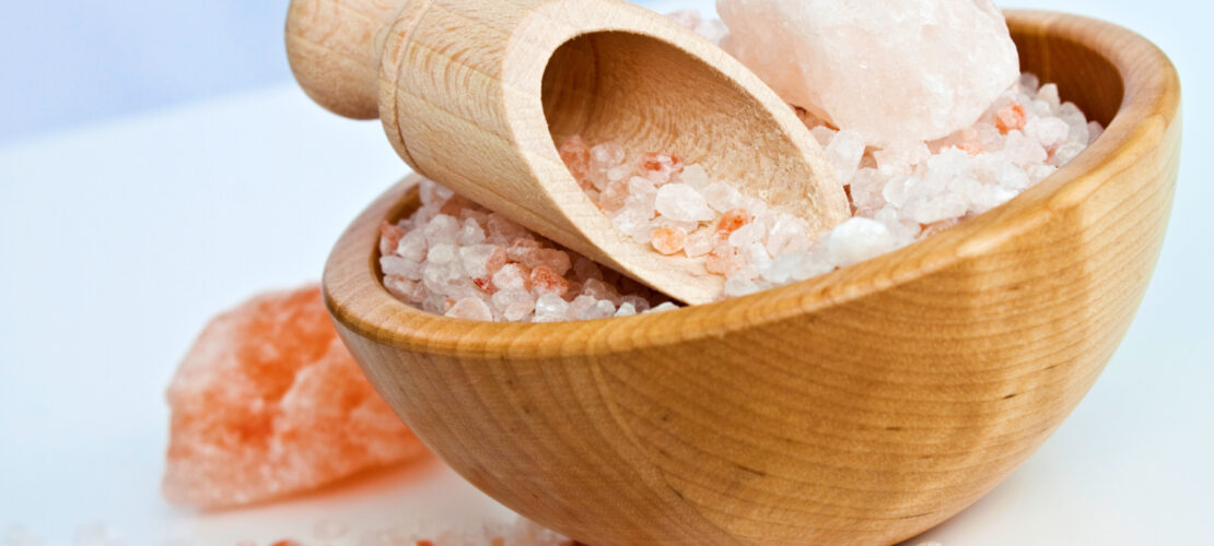 Eine Holzschüssel mit einem Holzlöffel auf Hellem Hintergrund. Die Schüssel ist mit Hellem Pinken Salz gefüllt